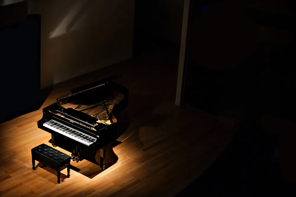 A grand piano spotlit on a warm wooden stage